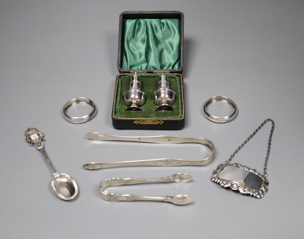 Small silver including a pair of Georgian sugar tongs, cased pepperettes, two napkin rings, spoon, tongs and wine label.